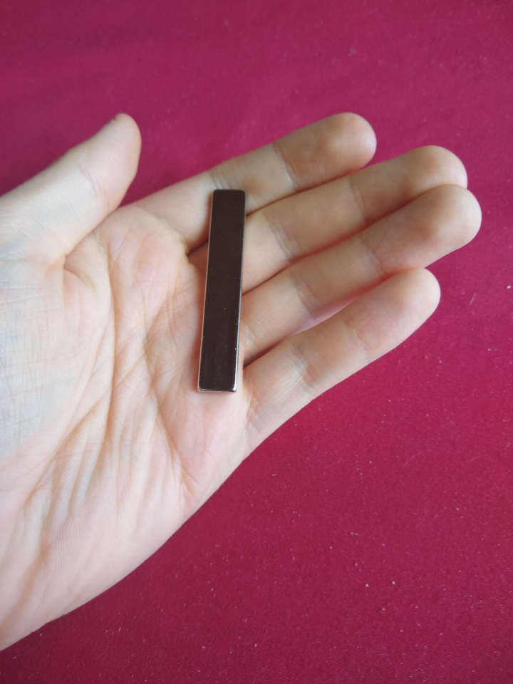 A hand holding a small metal bar (a magnet).