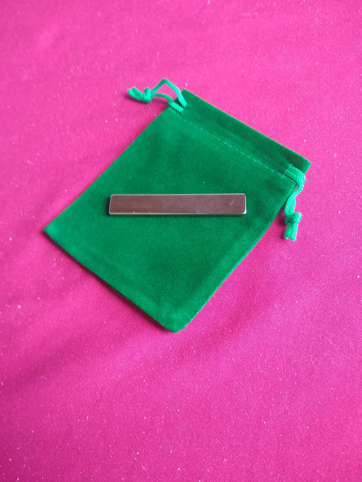 A small metal bar (a magnet) sitting on a small green bag with pull strings.