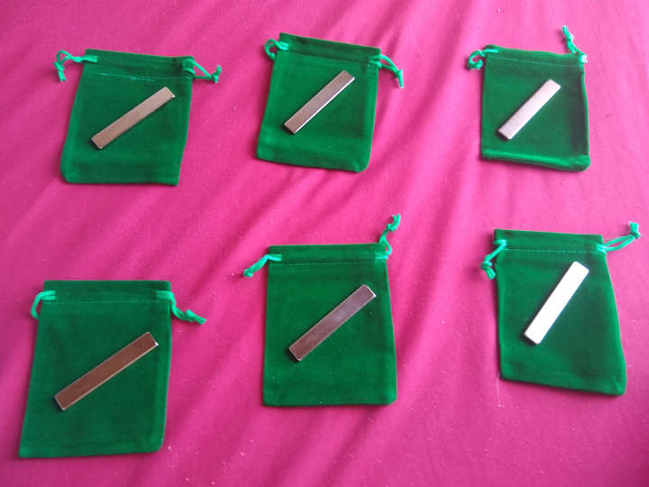 Six small metal bars (magnets) sitting on six small green bags with pullstrings.