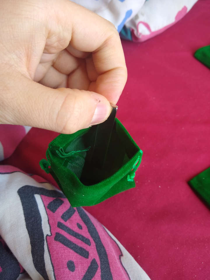 A small green bag with pull strings which is held open and a small metal bar (a magnet) being dropped in.