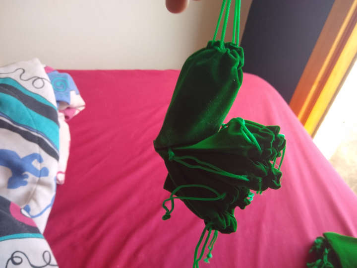 Several small green bags with pullstrings stuck together with one being held by the pullstrings and the others sticking to the first.
